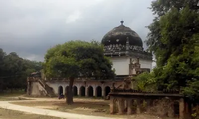 Colour photograph of a square domed tomb on a raised arcaded platform among trees, with steps and a low wall in front.