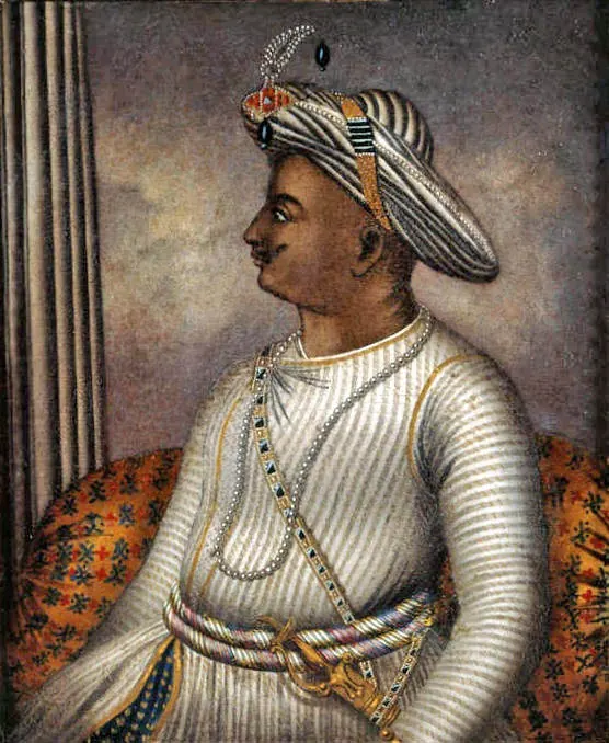 Painting of a man in profile seated against a patterned bolster, in a white robe and a striped turban with a jewelled ornament, a sword belt across his chest.
