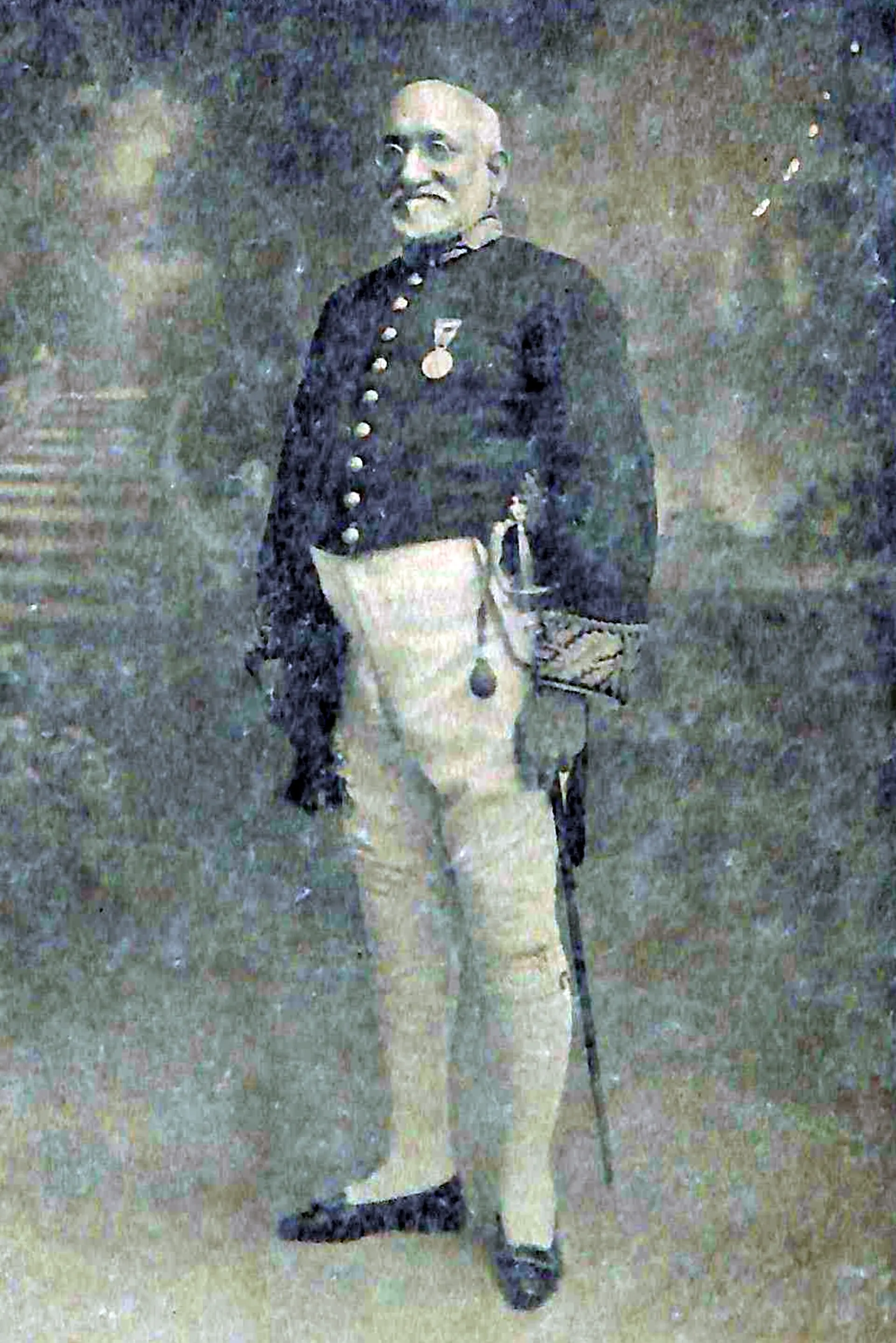 An old photograph of an elderly bearded man in a dark embroidered court coat with medals, white trousers and a sword, standing against a plain background.