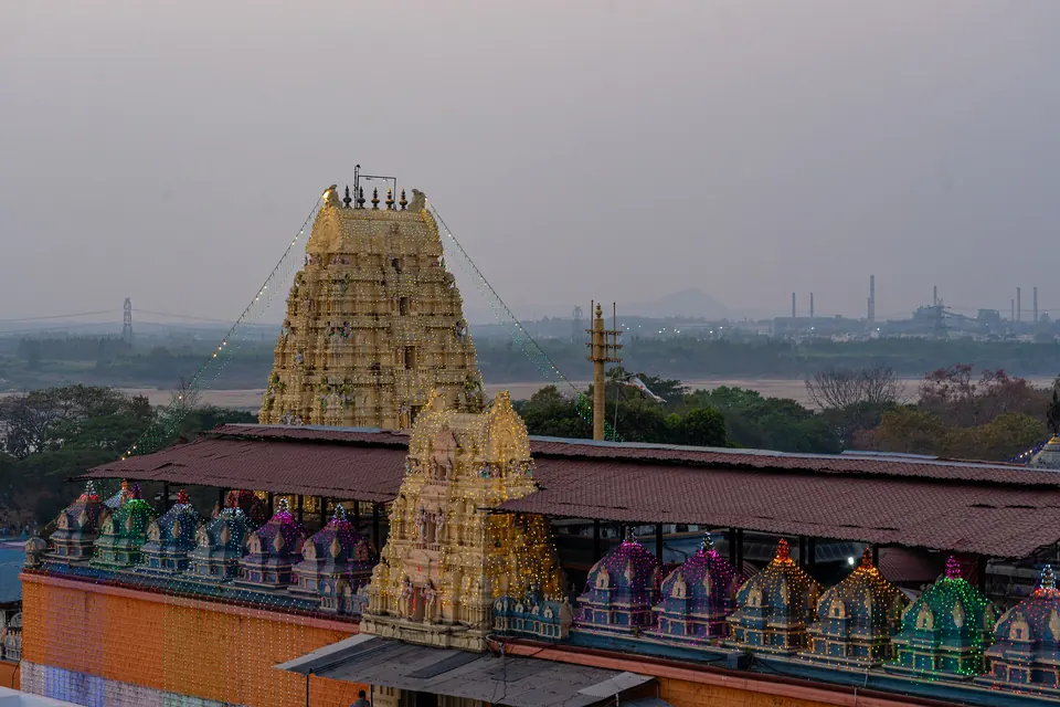 A temple complex with a tall golden gateway tower, smaller painted towers and long halls with orange walls, seen from a rooftop, with the town and hazy hills behind.