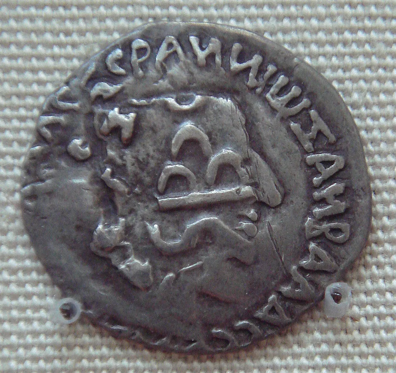 A worn round silver coin seen close up against a dark background, with faint traces of a head and letters under newer stamped symbols.