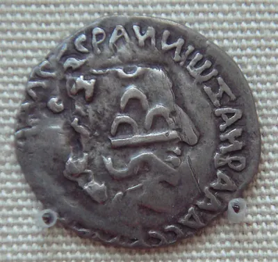 A worn round silver coin seen close up against a dark background, with faint traces of a head and letters under newer stamped symbols.