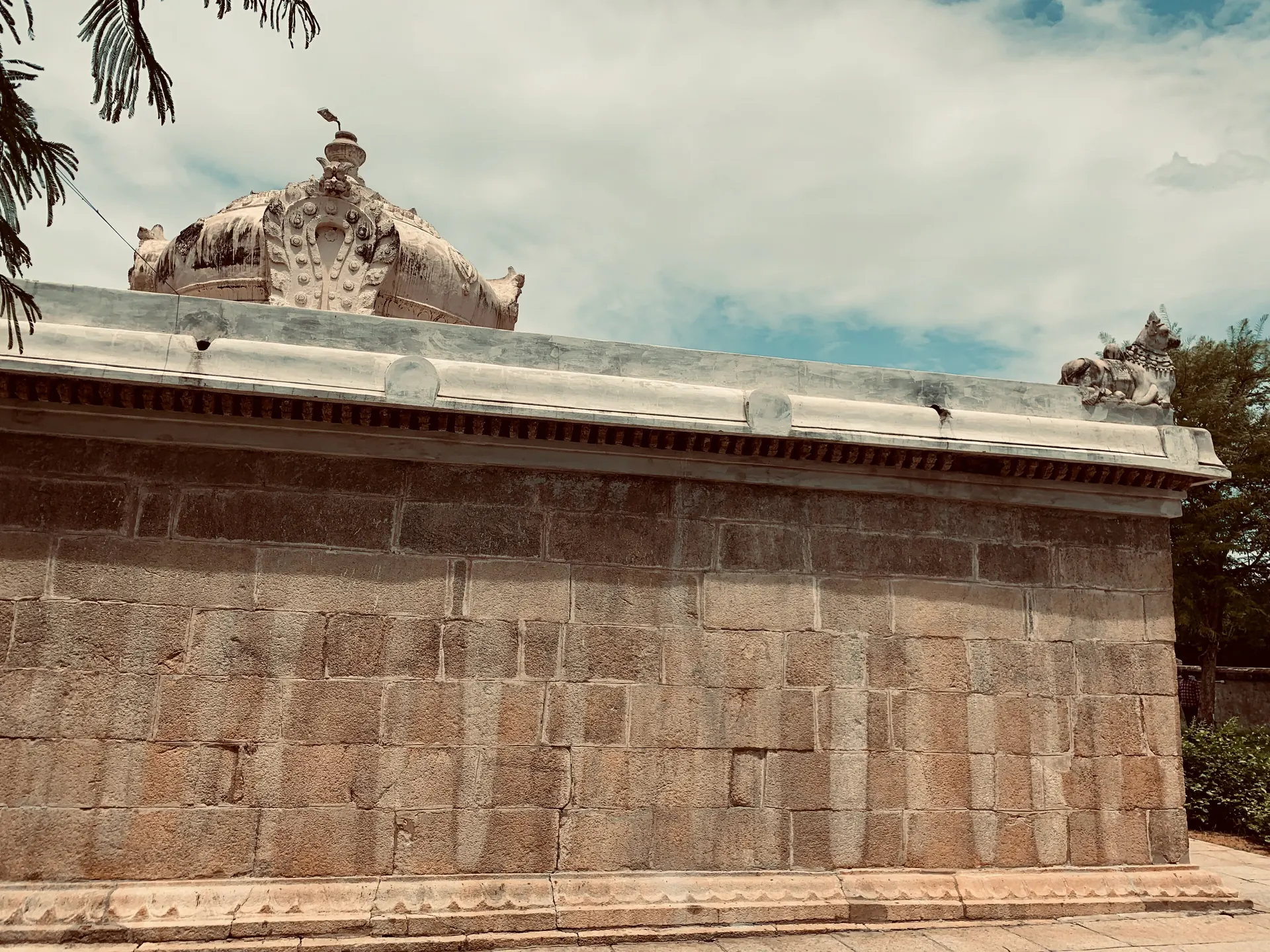 A long low wall of large stone blocks with a plain moulding, and a small domed tower rising behind it among trees.