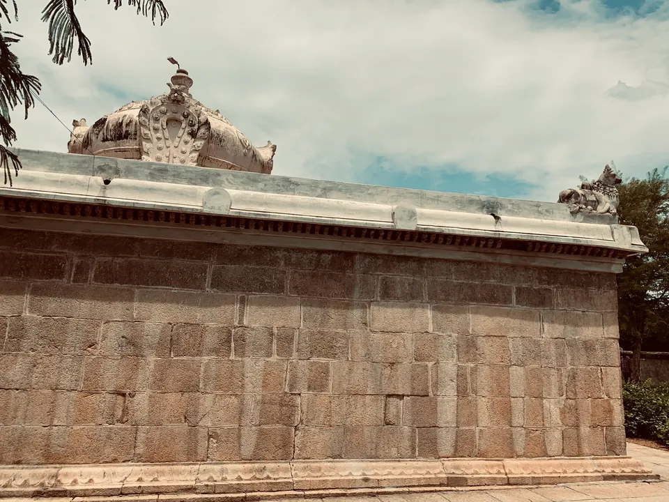 A long low wall of large stone blocks with a plain moulding, and a small domed tower rising behind it among trees.