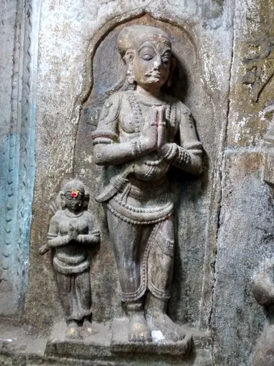 A stone relief of a man with a tall turban and a moustache, standing with hands joined in greeting, and a small woman beside him doing the same.