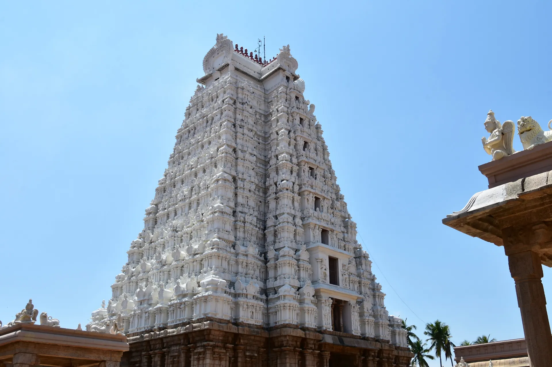 A tall white stepped temple gateway tower covered in rows of sculpted figures, under a clear blue sky.