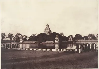 An old photograph of a wide square tank of still water with a striped low wall in front; a temple tower and small pavilions rise from the island in the middle.