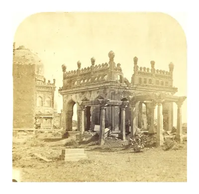 Old photograph of a ruined open pavilion of pointed arches on a terrace, with a carved grave in front.