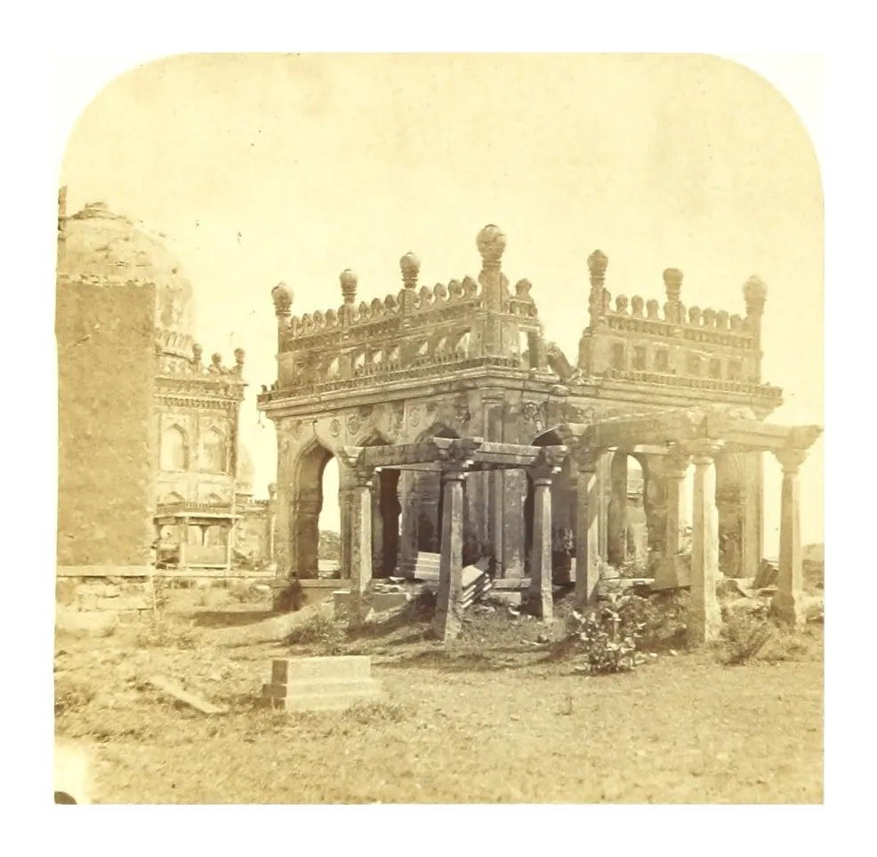 Old photograph of a ruined open pavilion of pointed arches on a terrace, with a carved grave in front.