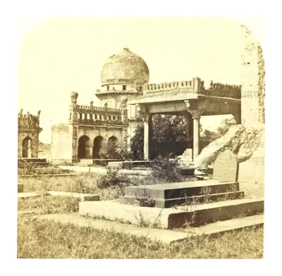 Old photograph of a domed tomb behind an arcaded building, with a broken grave in the foreground.