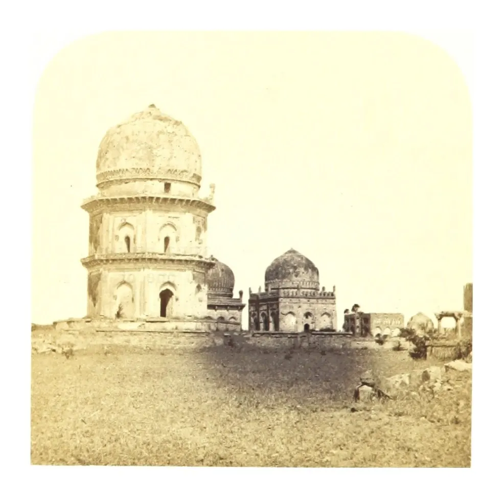 Old photograph of a tall domed tomb on a terrace with smaller domes beside it on open ground.