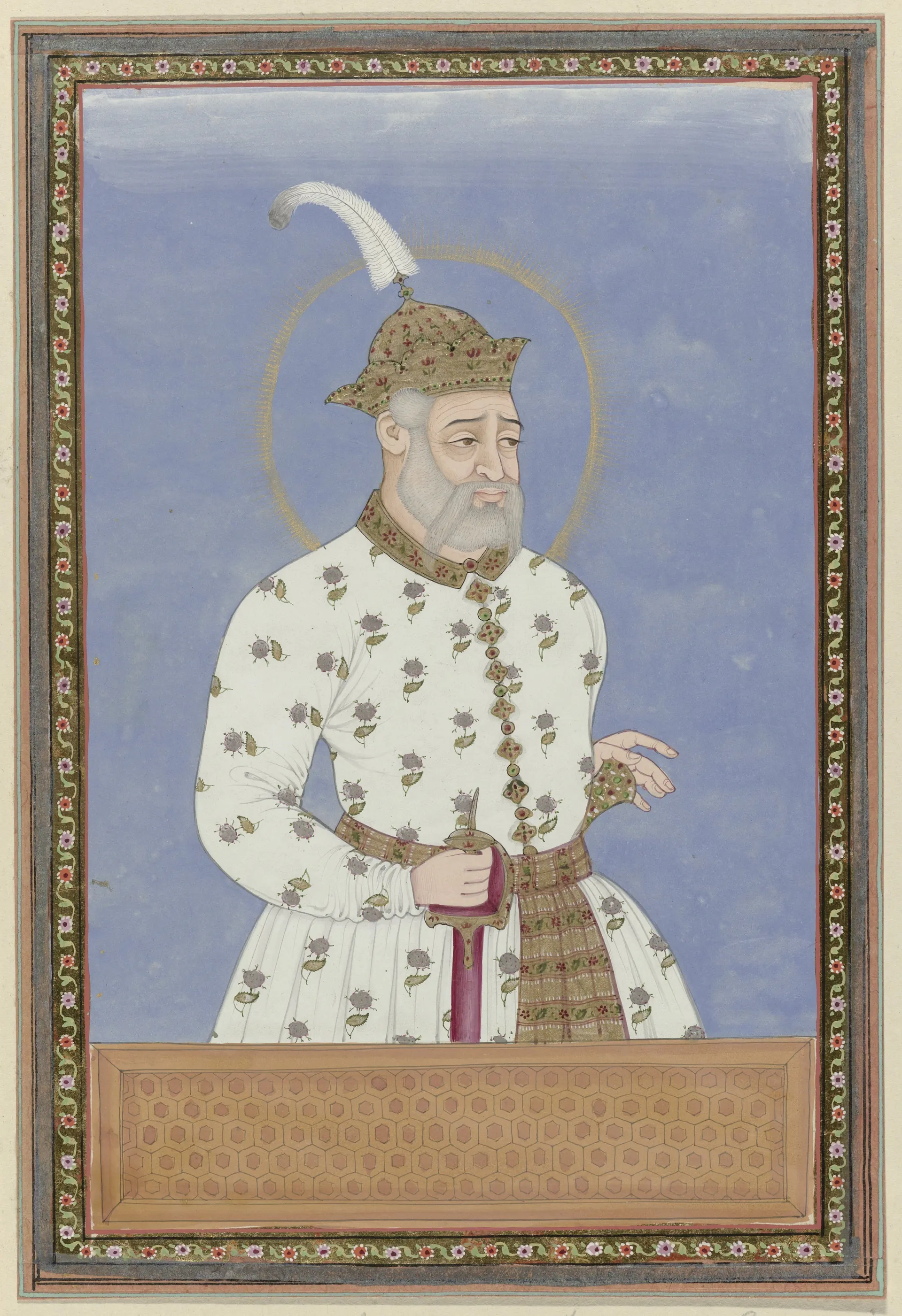 Deccani painting of a white-bearded man in a long white robe and a white turban with a plume, standing against a blue ground with a halo round his head, in a decorated border.