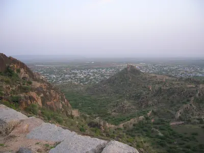 Colour photograph from a rocky hilltop looking down over scrub-covered hills to the town of Devarakonda spread across the plain.