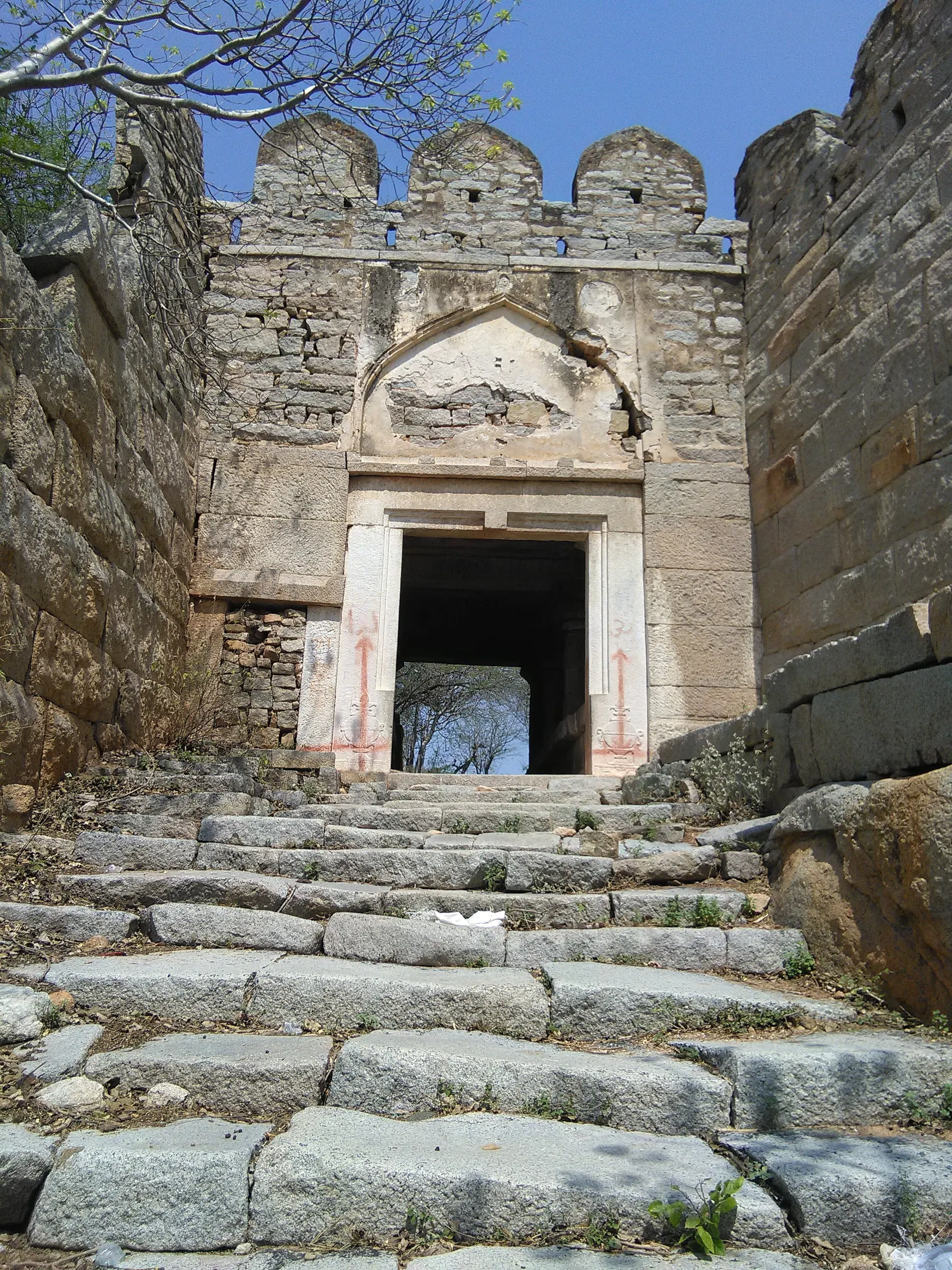 Colour photograph of a battlemented stone gateway with an arched panel over a square doorway, reached by a broad flight of worn granite steps.