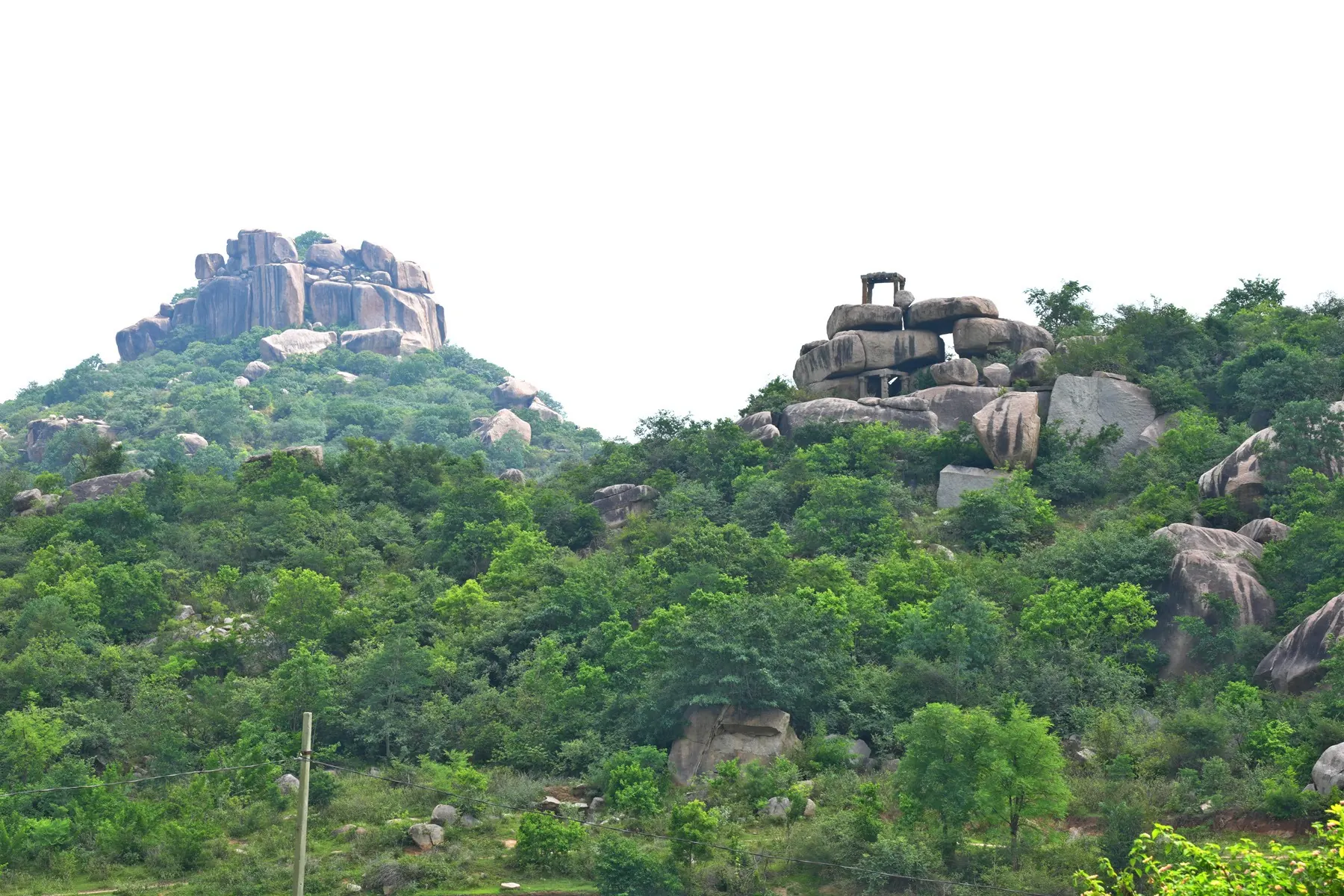Colour photograph of two wooded hills crowned with piles of granite boulders, a small stone structure standing on the summit of the right-hand hill.