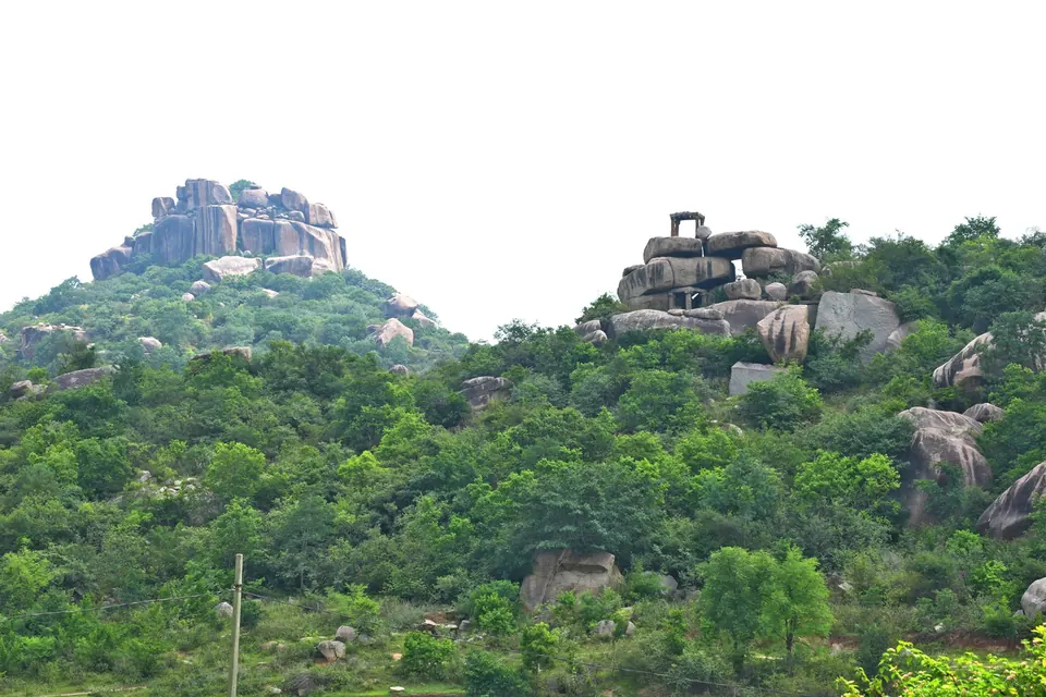 Colour photograph of two wooded hills crowned with piles of granite boulders, a small stone structure standing on the summit of the right-hand hill.