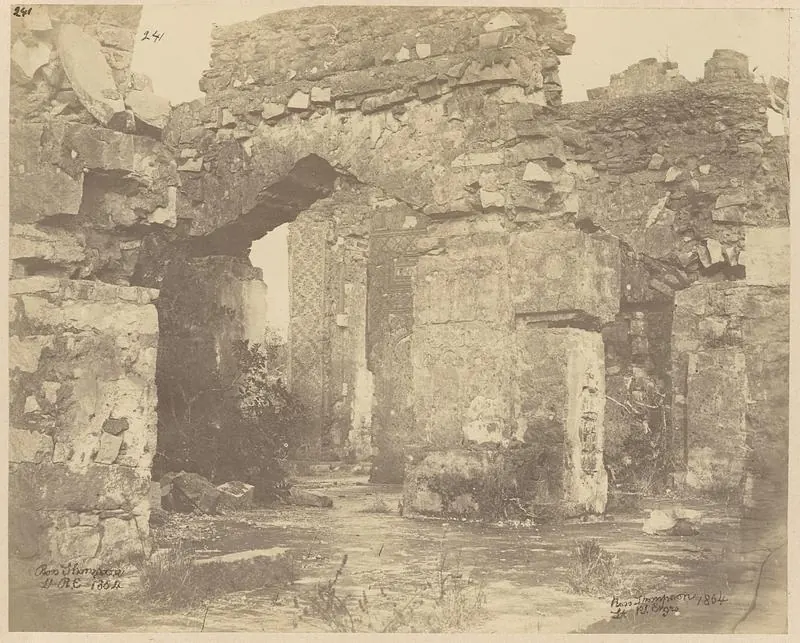 Sepia photograph of a ruined stone building with a tall arched opening, rubble walls and carved pillars, weeds growing in front; signed and dated 1864 in the corners.