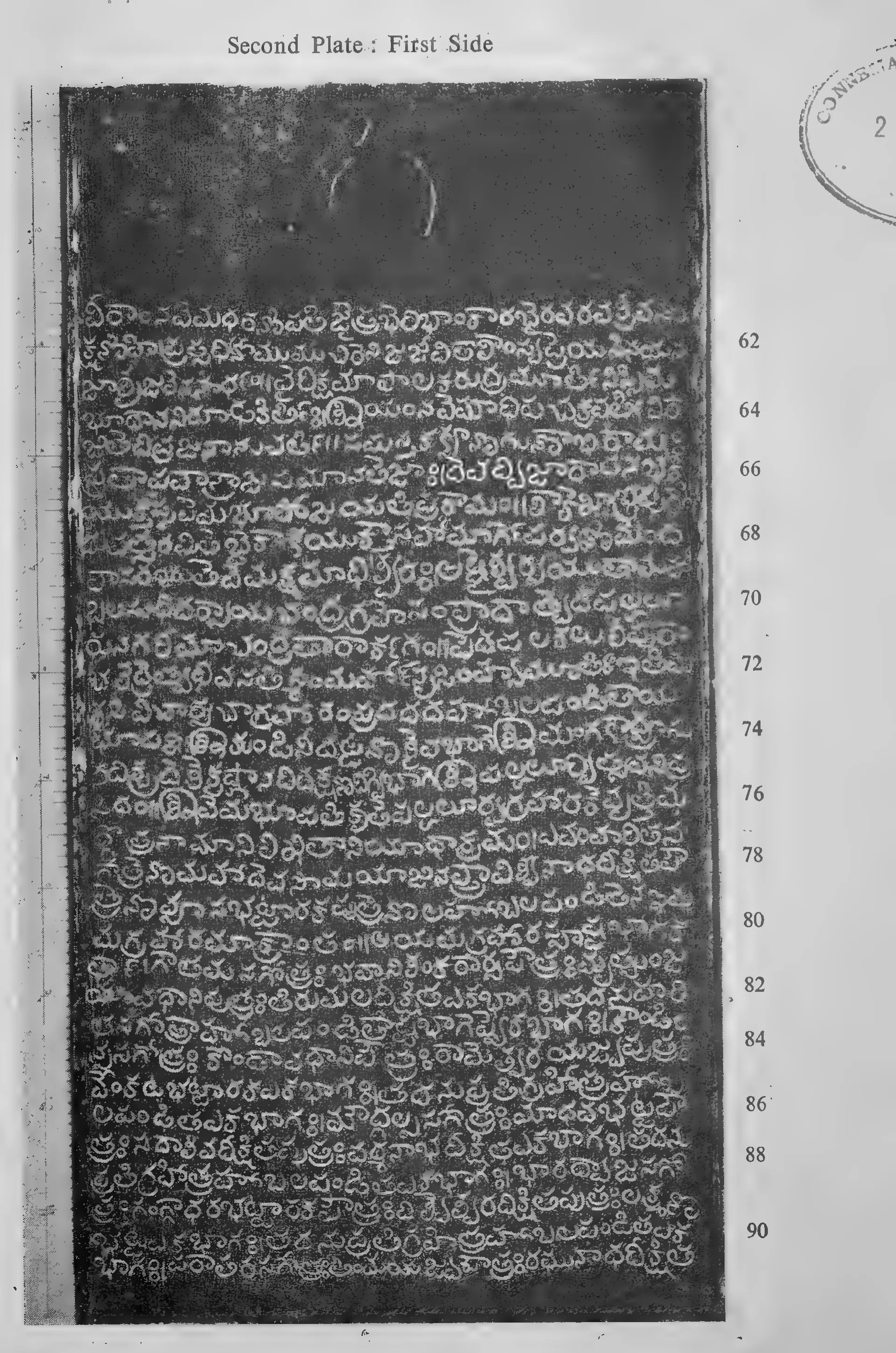 Photograph of one inscribed copper-plate face, upright and narrow, about thirty lines of light Telugu letters on the dark metal, with a raised rim and the ring hole at one end; line numbers printed in the margin.