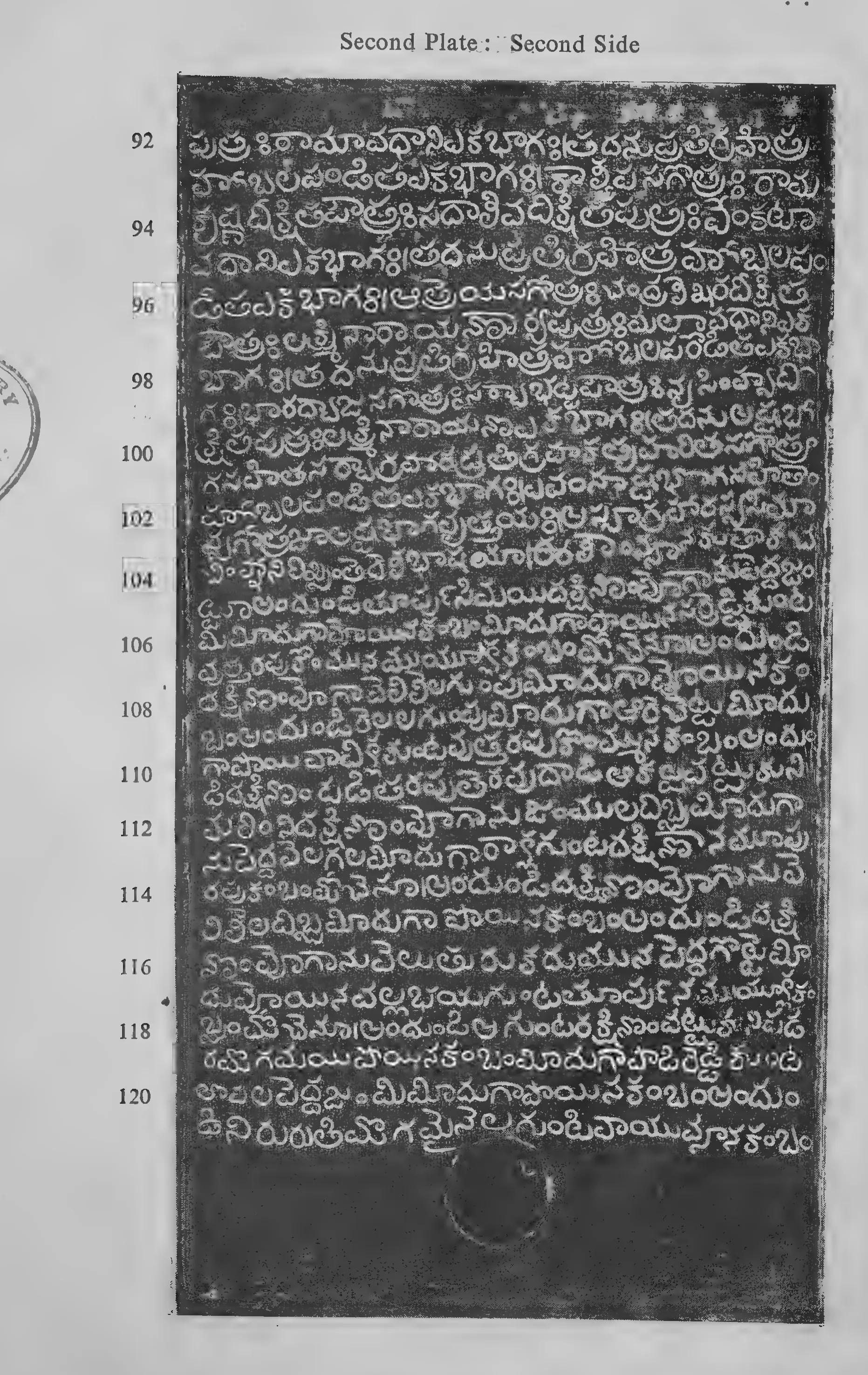 Photograph of one inscribed copper-plate face, upright and narrow, about thirty lines of light Telugu letters on the dark metal, with a raised rim and the ring hole at one end; line numbers printed in the margin.