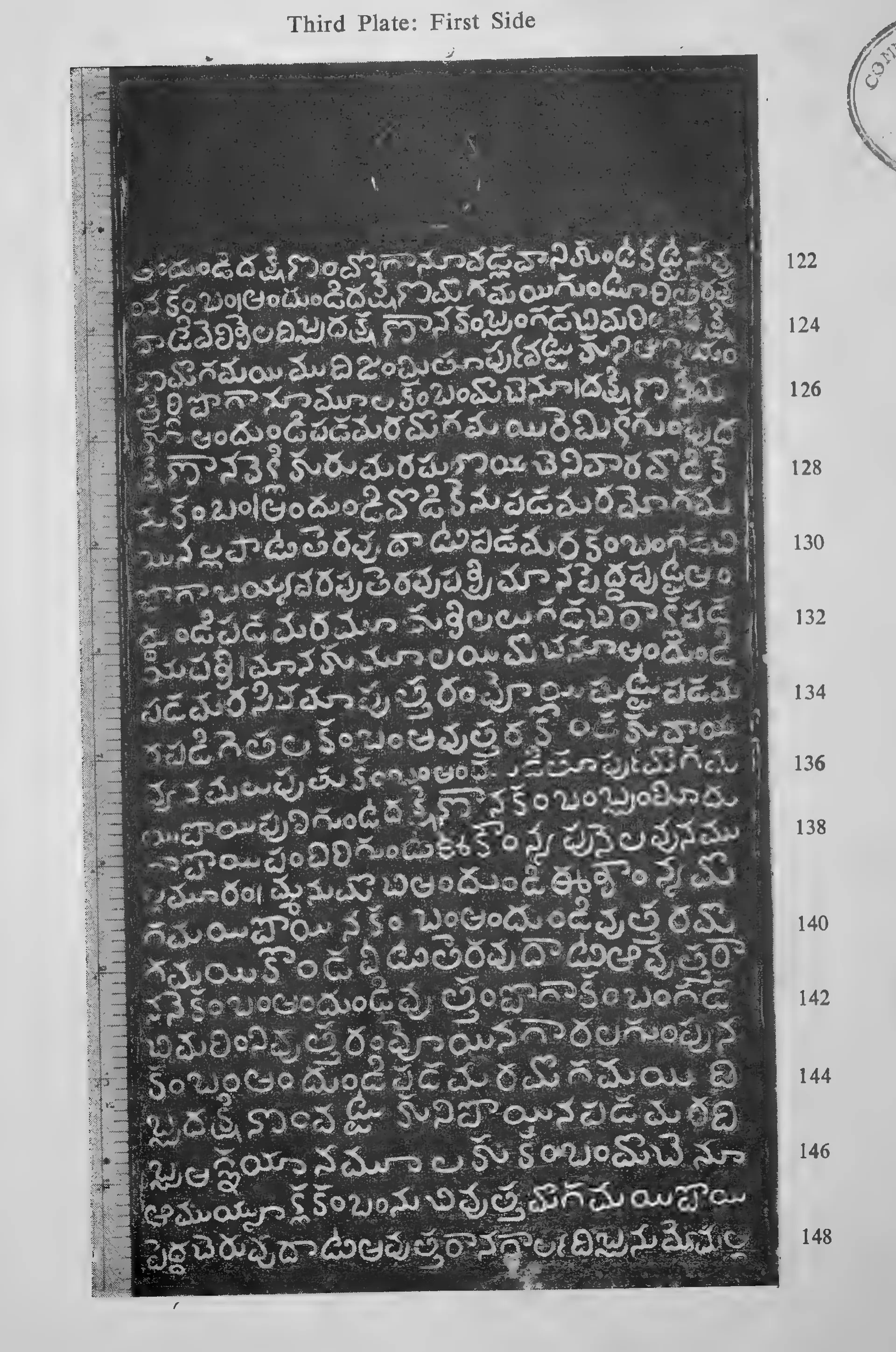 Photograph of one inscribed copper-plate face, upright and narrow, about thirty lines of light Telugu letters on the dark metal, with a raised rim and the ring hole at one end; line numbers printed in the margin.