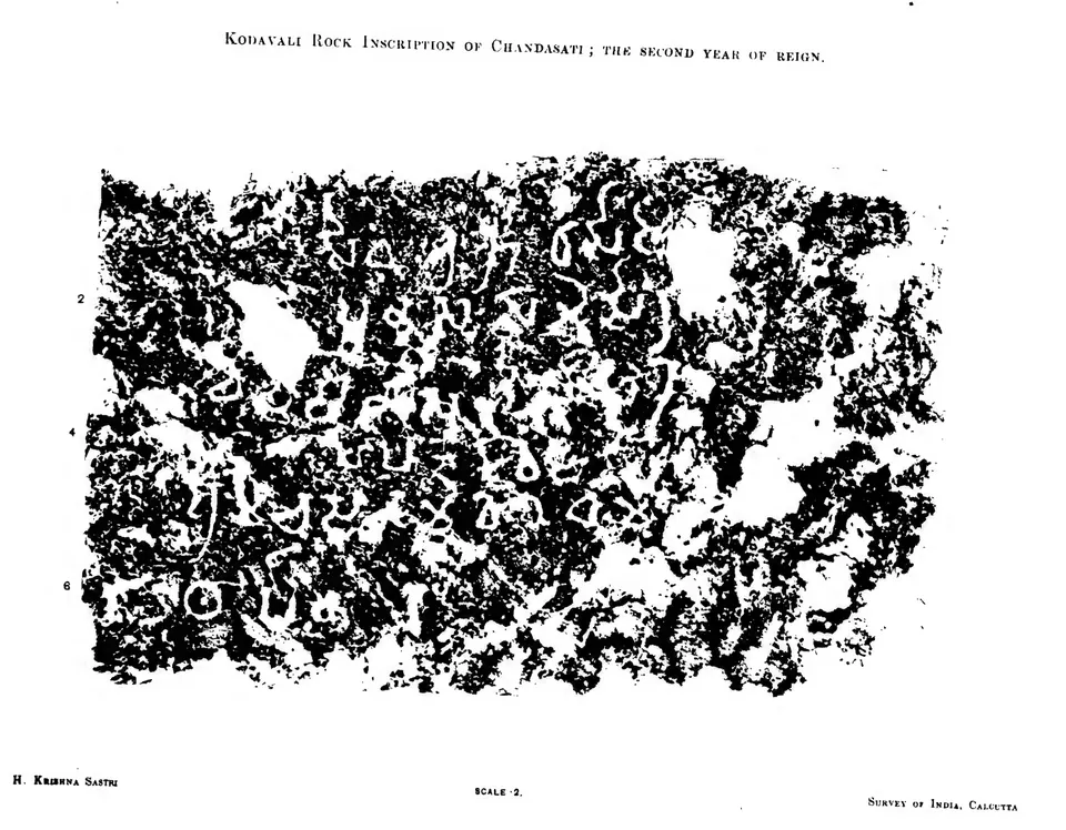 Ink impression of six lines of large, rounded Brahmi letters cut into rough rock, white on a speckled black ground, with patches where the rock surface has flaked away.