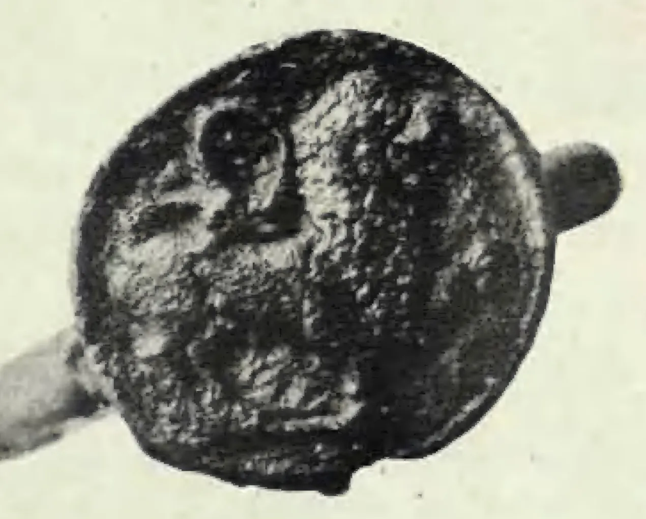 Photograph of a round seal soldered to the ring that held the plates; a rampant maned animal in high relief, its left paw raised, fills the face of the seal.