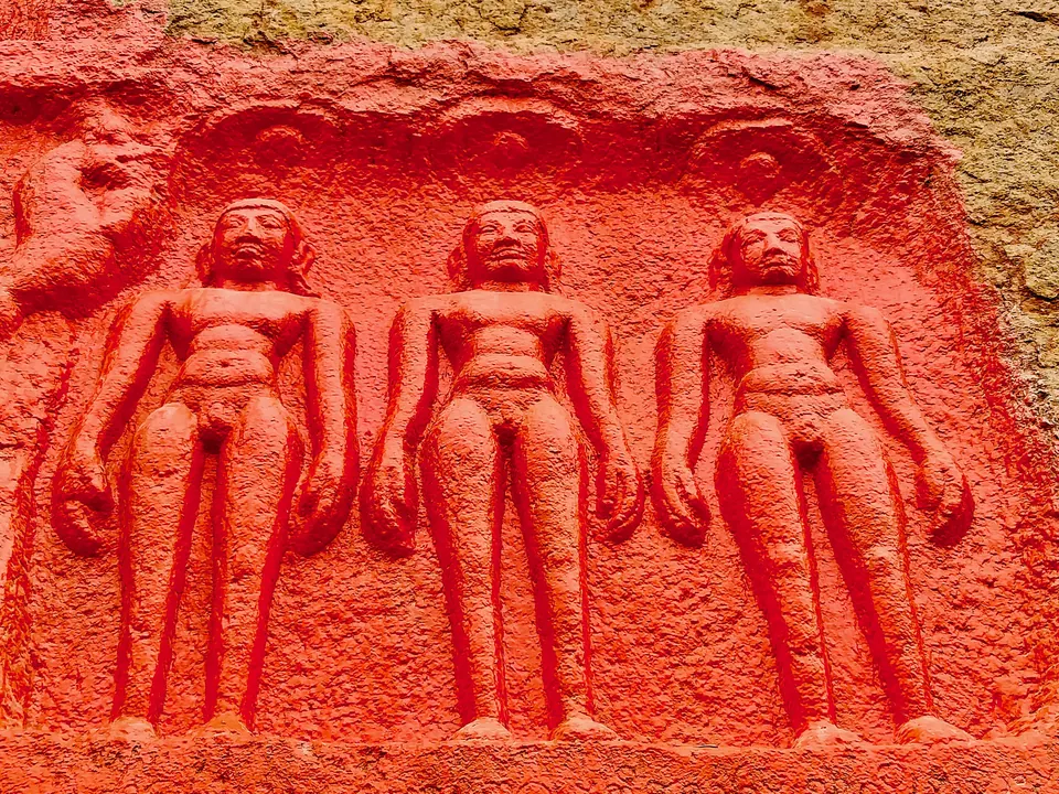 Panel of three standing nude Jaina figures carved side by side in a shallow niche on the rock, painted red.