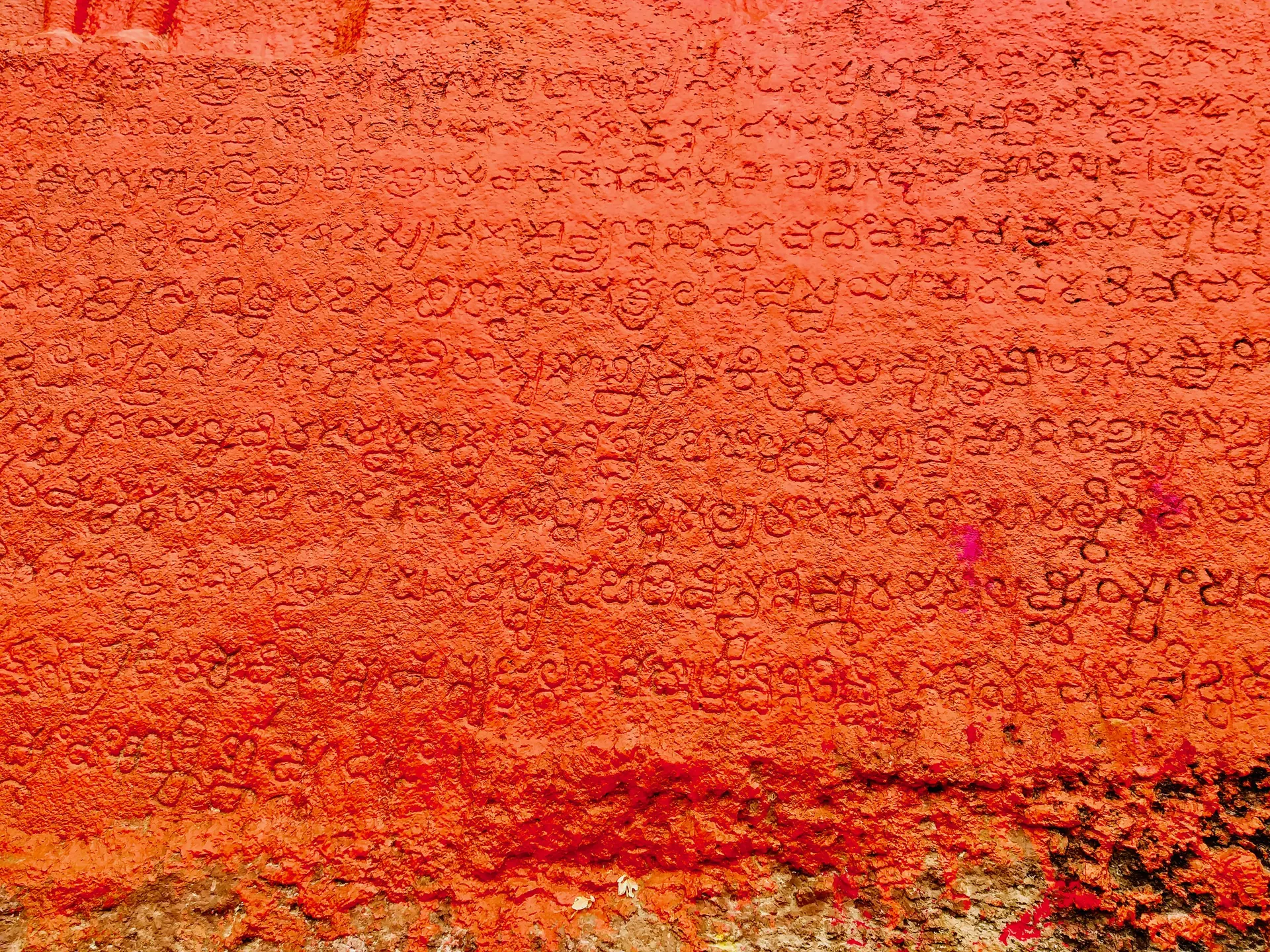 Part of the long inscription cut on the rock of the Bommala Gutta: rows of closely spaced Telugu-Kannada letters on a rock surface painted red.