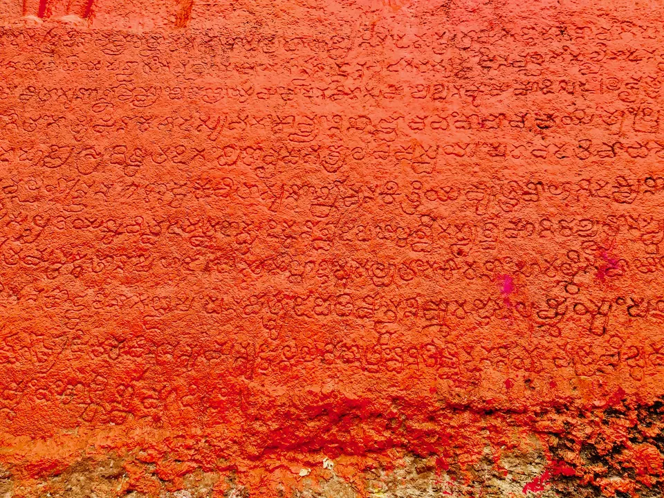 Part of the long inscription cut on the rock of the Bommala Gutta: rows of closely spaced Telugu-Kannada letters on a rock surface painted red.