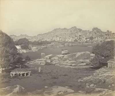 Albumen photograph of a long street lined with ruined stone pavilions and colonnades running towards boulder-strewn hills.