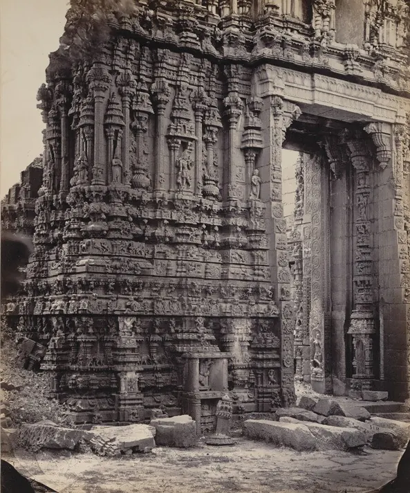 Albumen photograph of the richly carved stone lower storey of a temple gateway, its jambs and walls covered with figures and mouldings, fallen blocks in front.