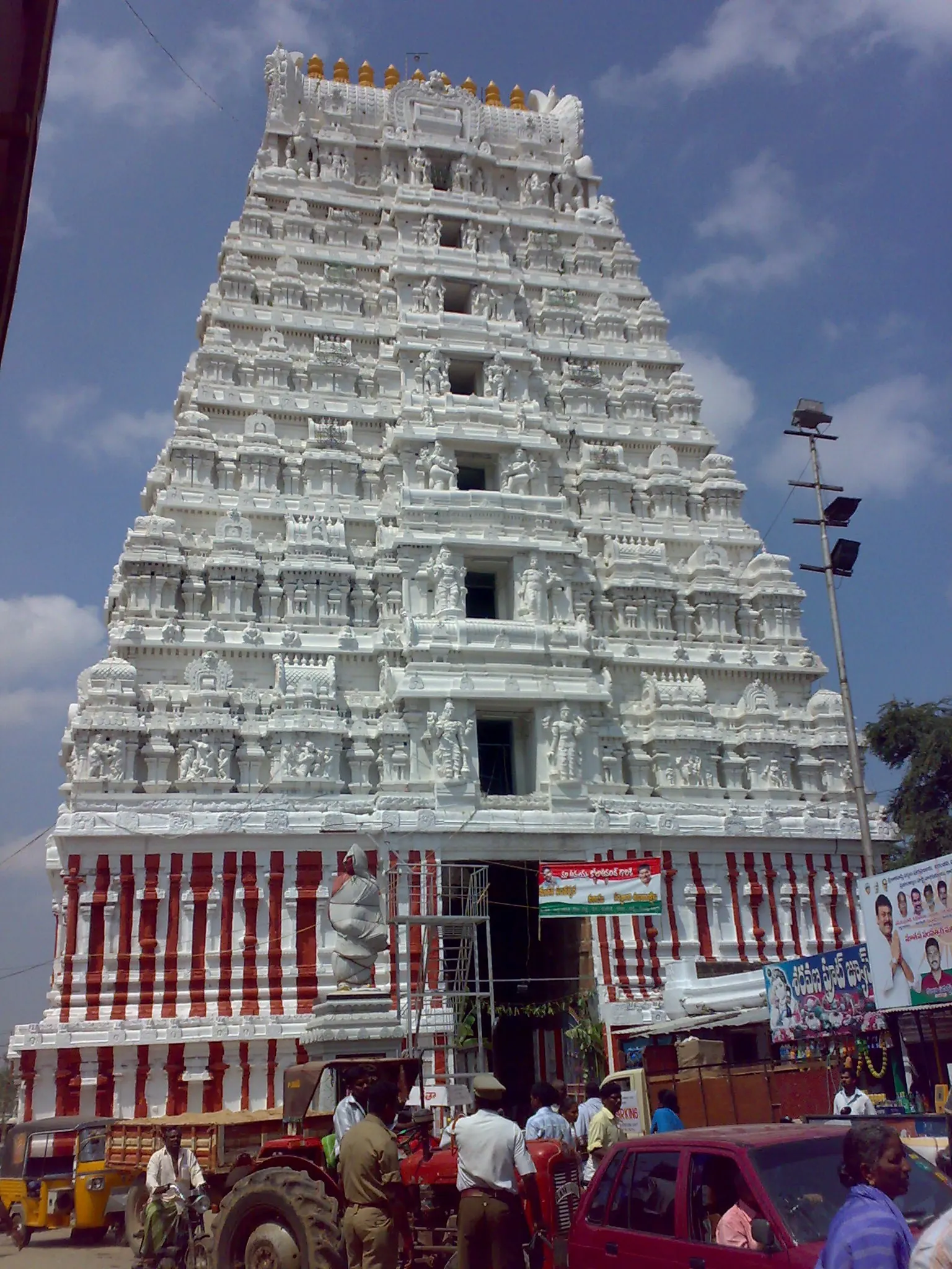 Colour photograph of a tall whitewashed temple gateway tower with many storeys of sculpture above a busy street.