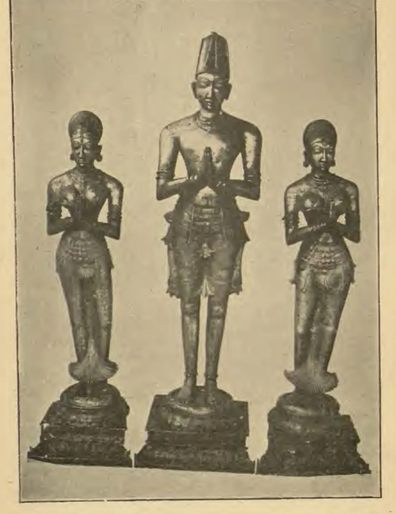 Photograph of three standing metal statues on round pedestals, hands joined in worship: a taller crowned king in the centre between two smaller crowned queens.