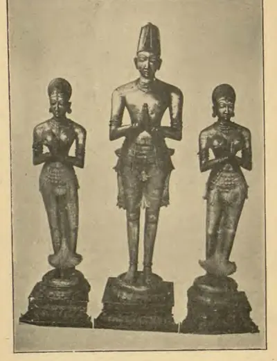 Photograph of three standing metal statues on round pedestals, hands joined in worship: a taller crowned king in the centre between two smaller crowned queens.