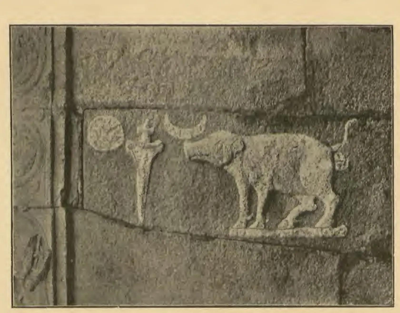 Photograph of a stone relief: a boar facing a standing dagger, with the sun and the crescent moon above. Printed sideways on the page.