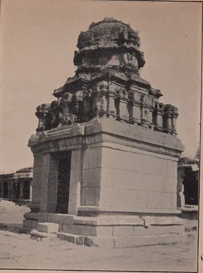 Photograph of a small square stone shrine with a plain doorway and a weathered tower, standing in a paved court.
