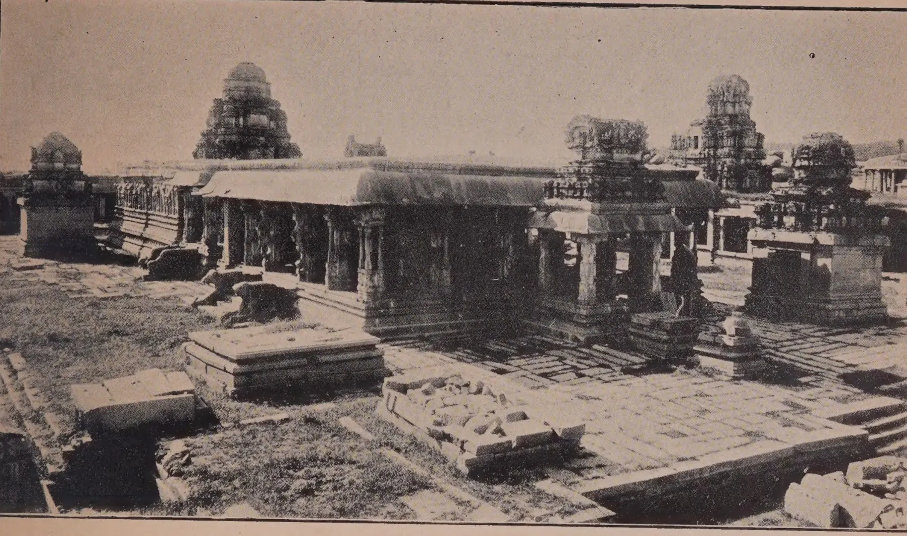 Photograph of the ruined courtyard of the Krishna temple at Hampi: a pillared hall and shrines with stepped towers, fallen stones in the foreground.
