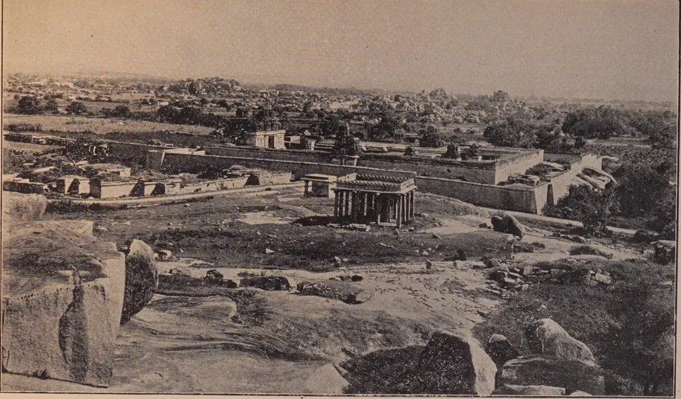 Photograph over boulders towards a walled temple enclosure with a pillared pavilion in front and the ruins of Vijayanagara beyond. Printed sideways.
